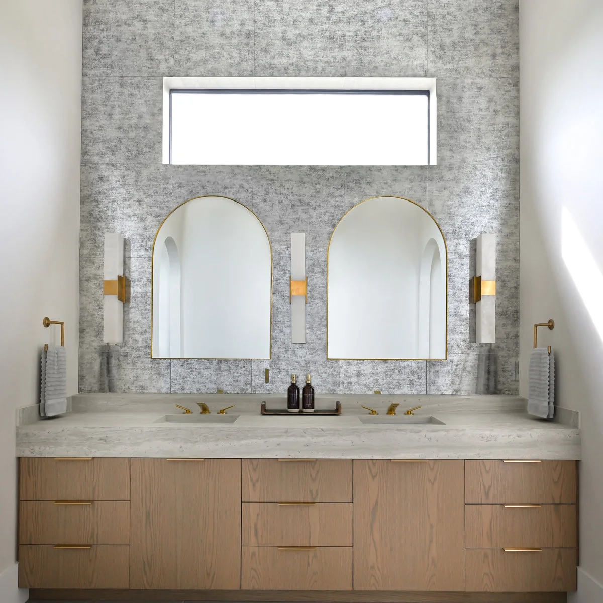Two gold-edged arched mirrors beneath a horizontal bathroom window