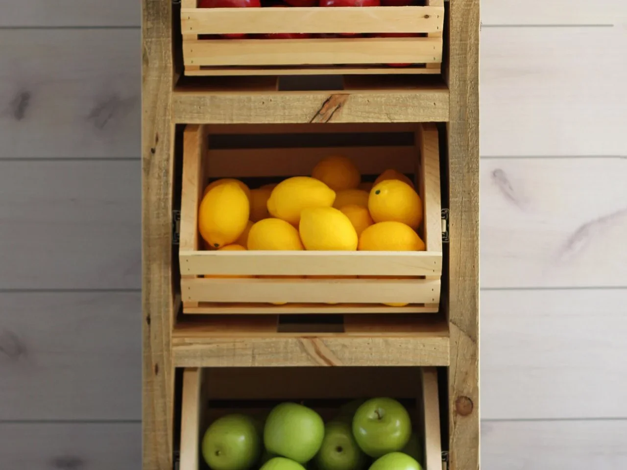 Small open timber crates filled with lemons and green apples sit inside a rough timber storage frame.