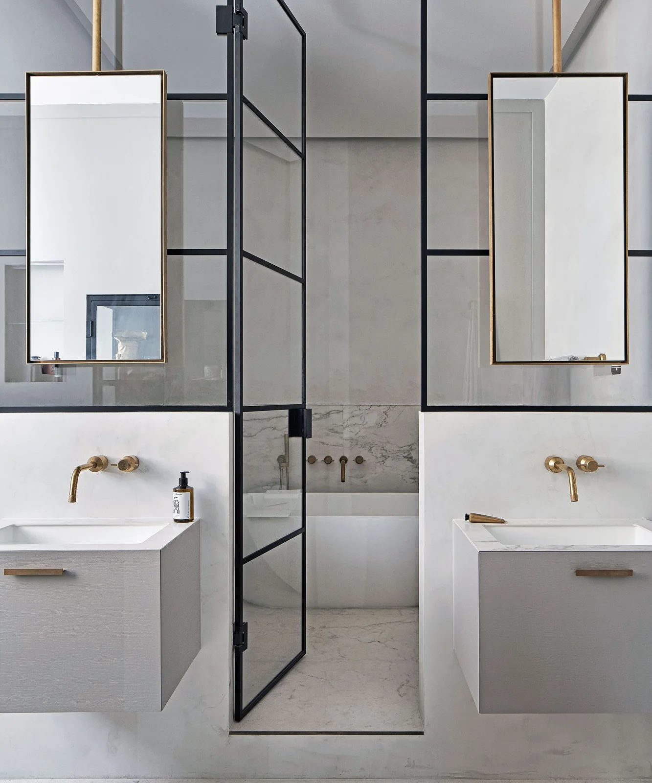 Two floating pale vanities and tall hanging mirrors stand beside dark-framed glazed doors leading to a white bath against pale walls