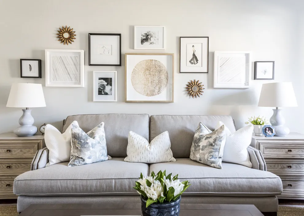 Pale and dark frames are grouped with small round decorative pieces above a gray sofa