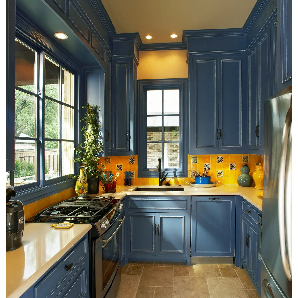 Blue kitchen cabinets surrounding a yellow tile backsplash with scattered decorative patterned tiles