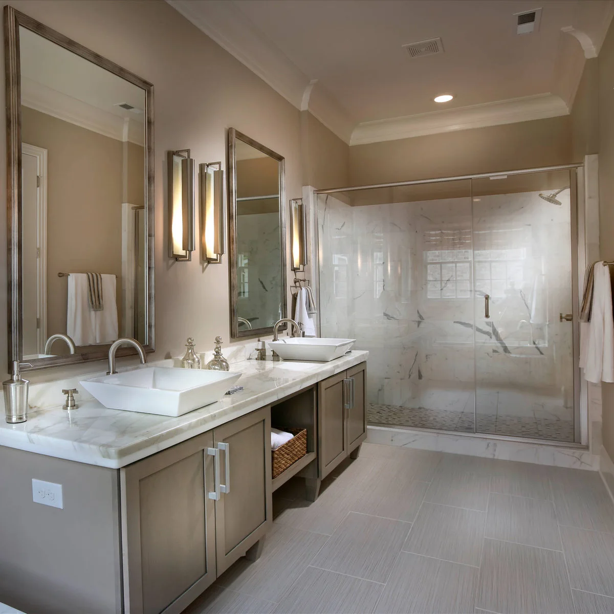 Two low white rectangular vessel sinks line a pale counter above gray cabinets, with tall mirrors and narrow wall lights.