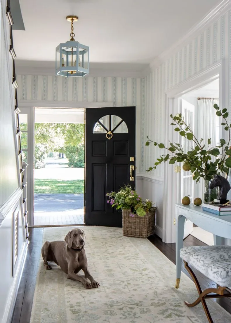 Pale blue candle lantern over striped entry with black door, pale blue console, patterned rug and white paneling