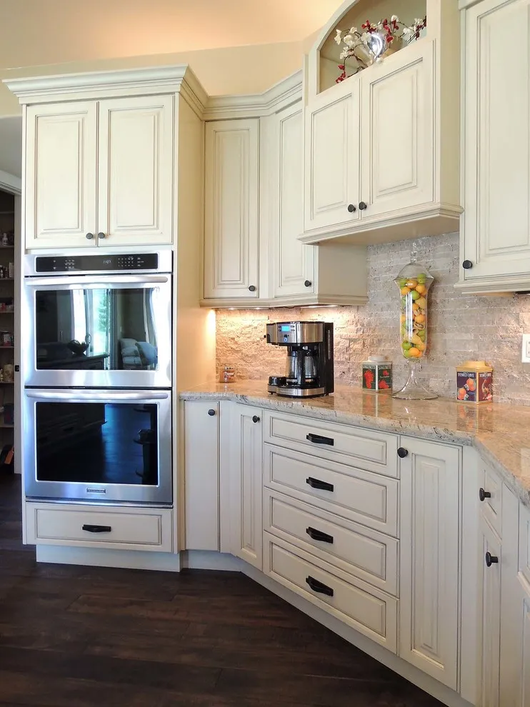 Warm white paneled cabinets surround built-in ovens above dark flooring