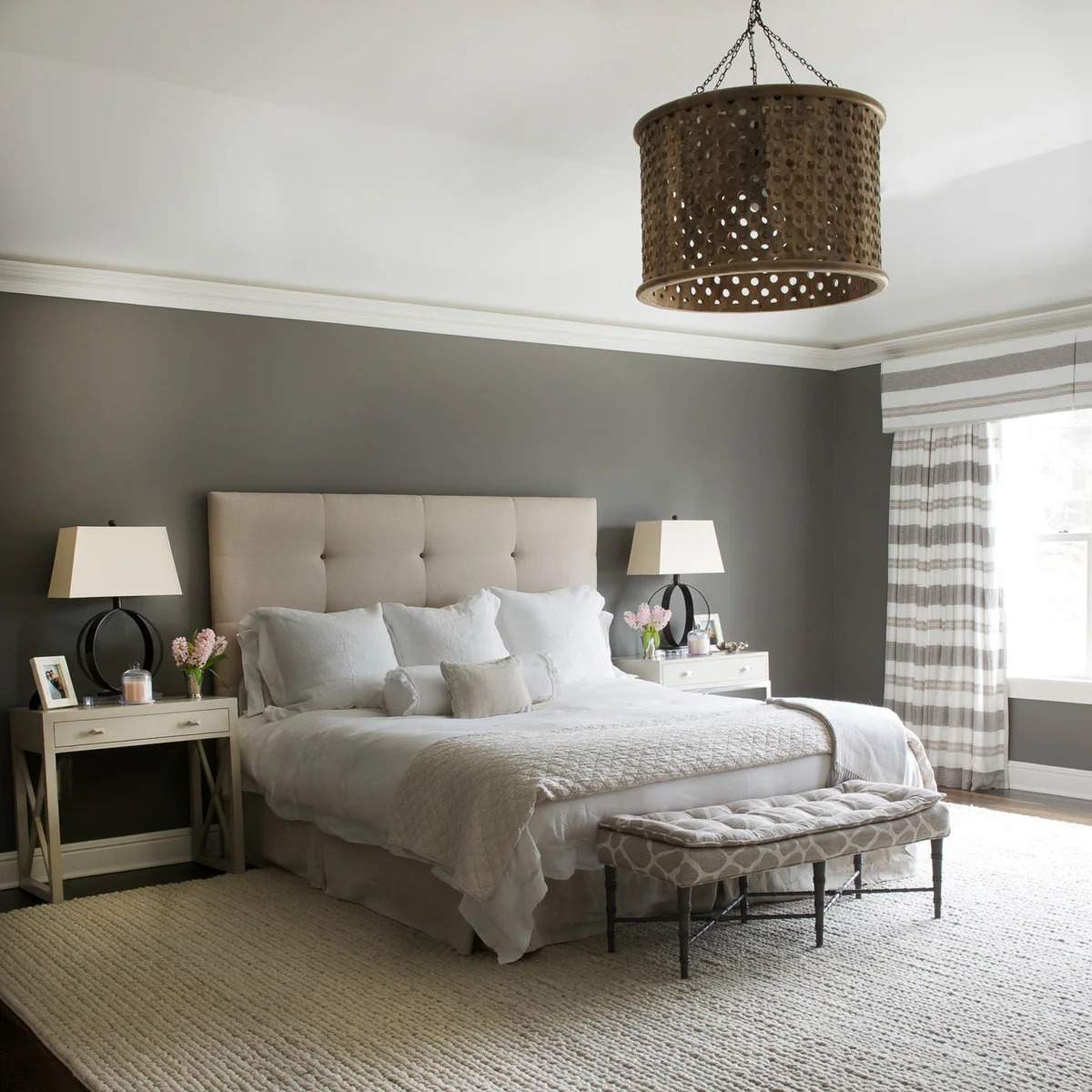 A large cream textured rug extends beside a pale bed and beneath a patterned bench in a gray bedroom.