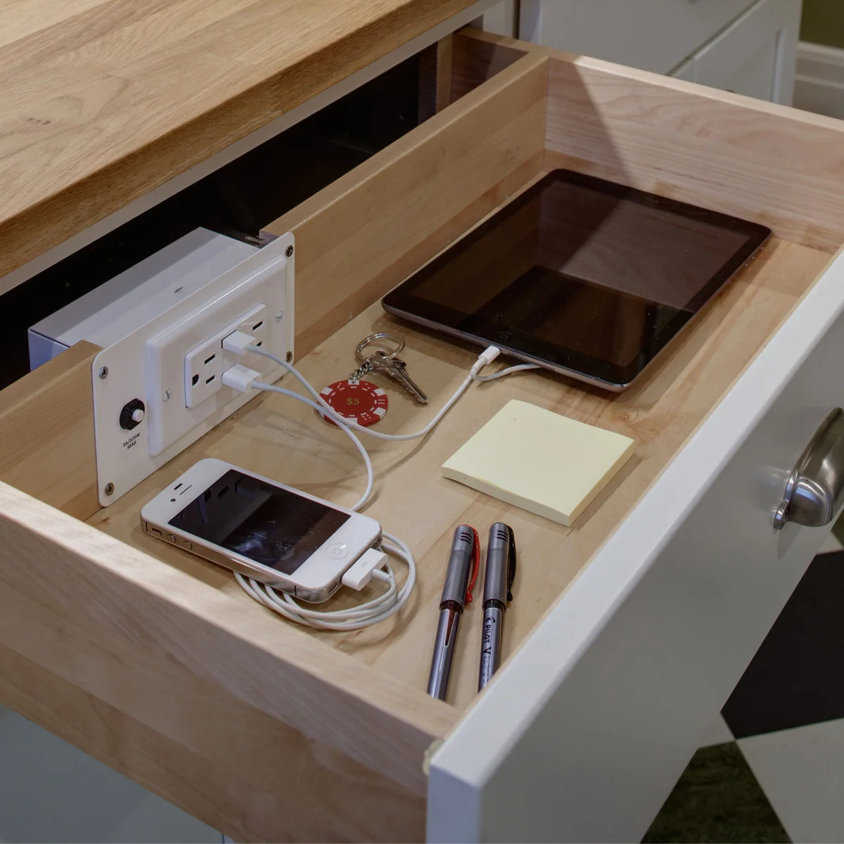 Shallow wooden drawer with a phone, tablet, keys, pens, sticky notes and a built-in charging outlet
