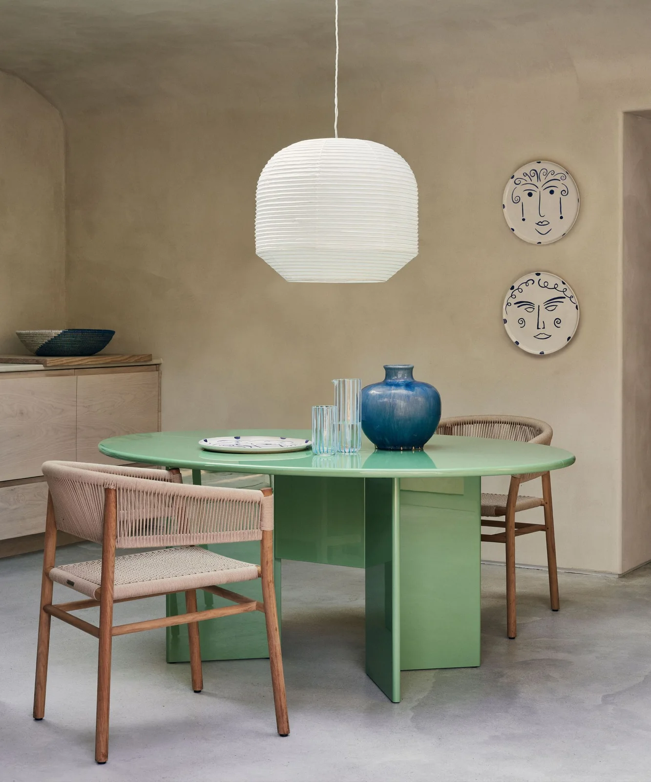 A mint-green round pedestal table sits beside pale wooden chairs, neutral walls and a white hanging light