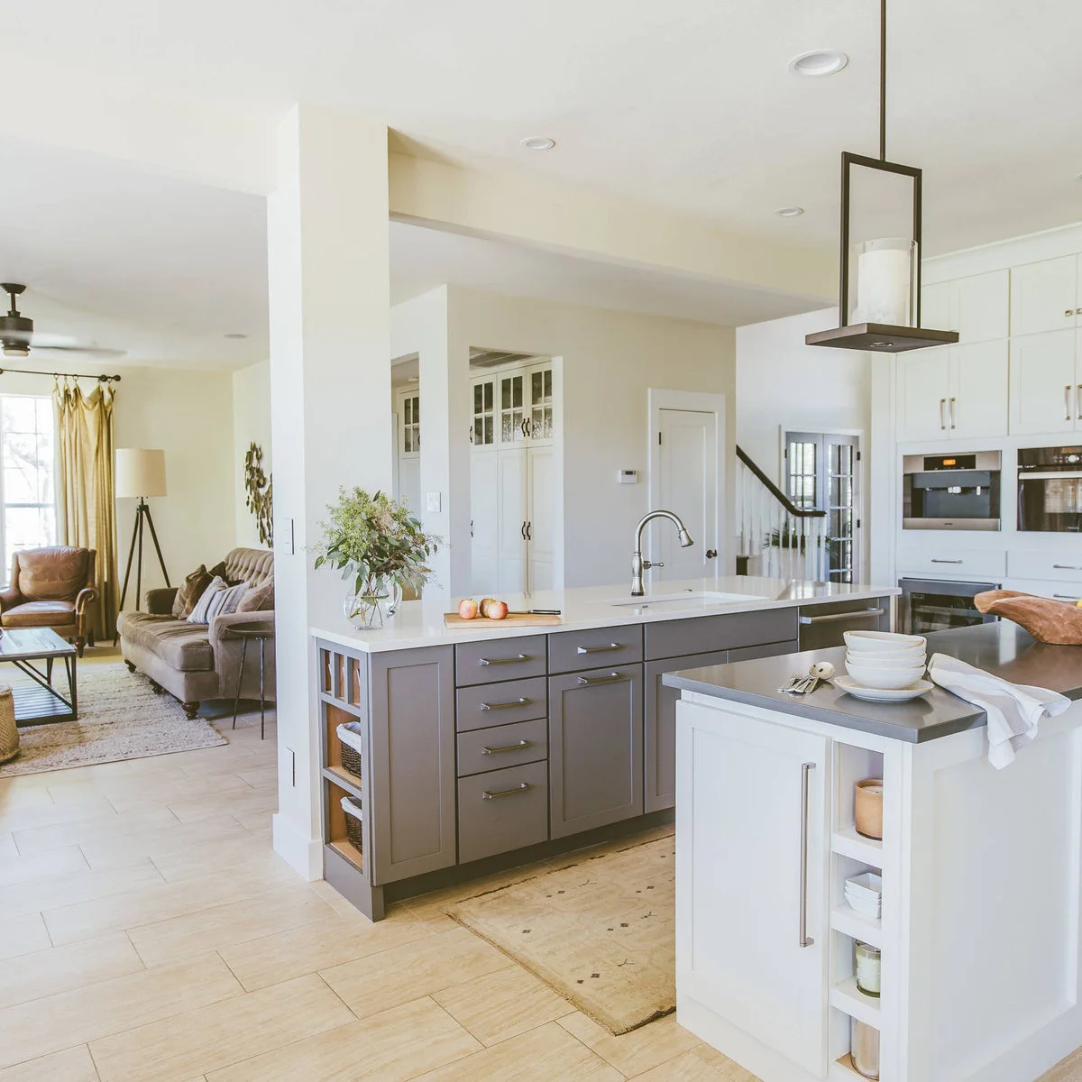 A gray sink cabinet and tall white post divide a kitchen from a living area with brown seating.