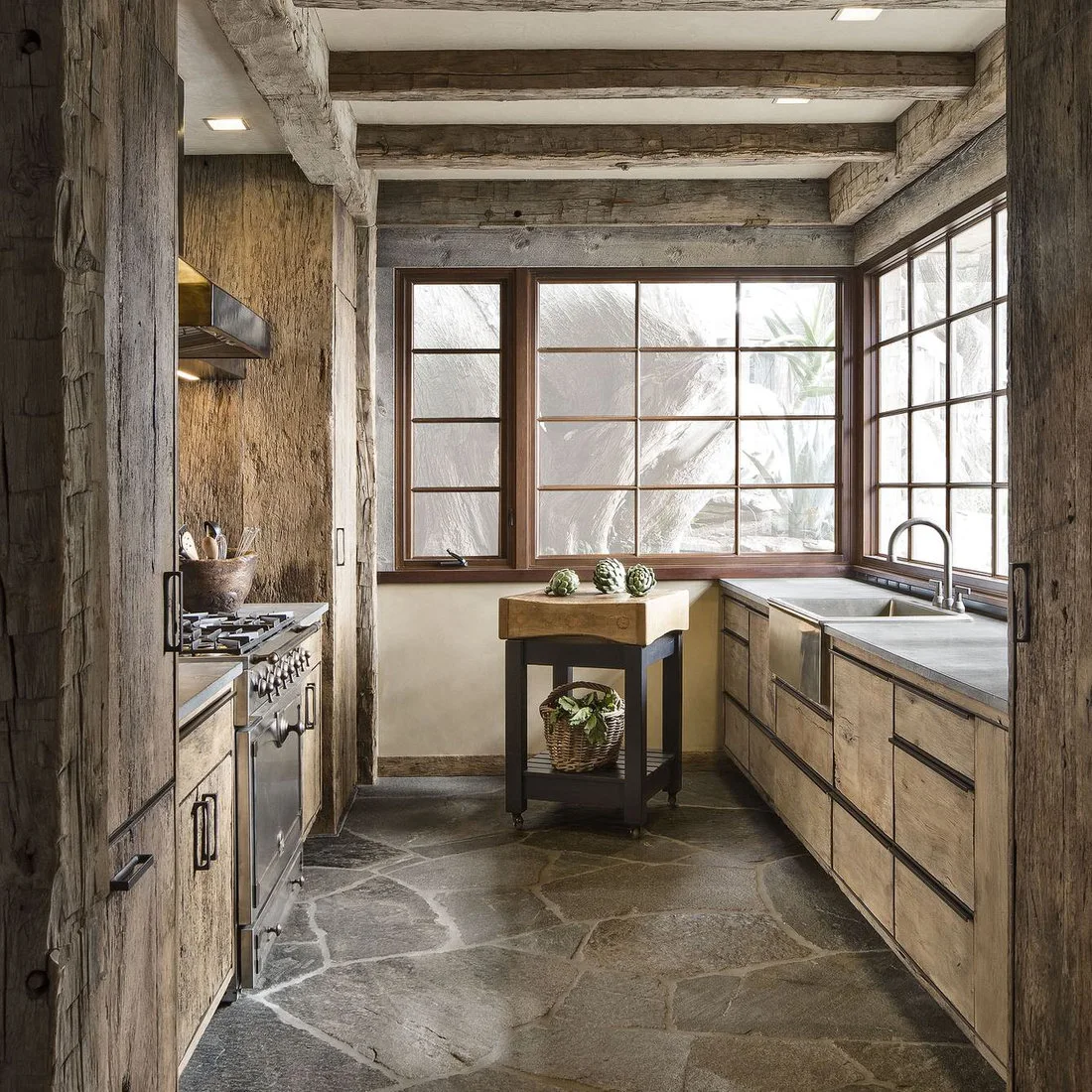 A compact timber kitchen with stone floor, corner windows and a small butcher block stand