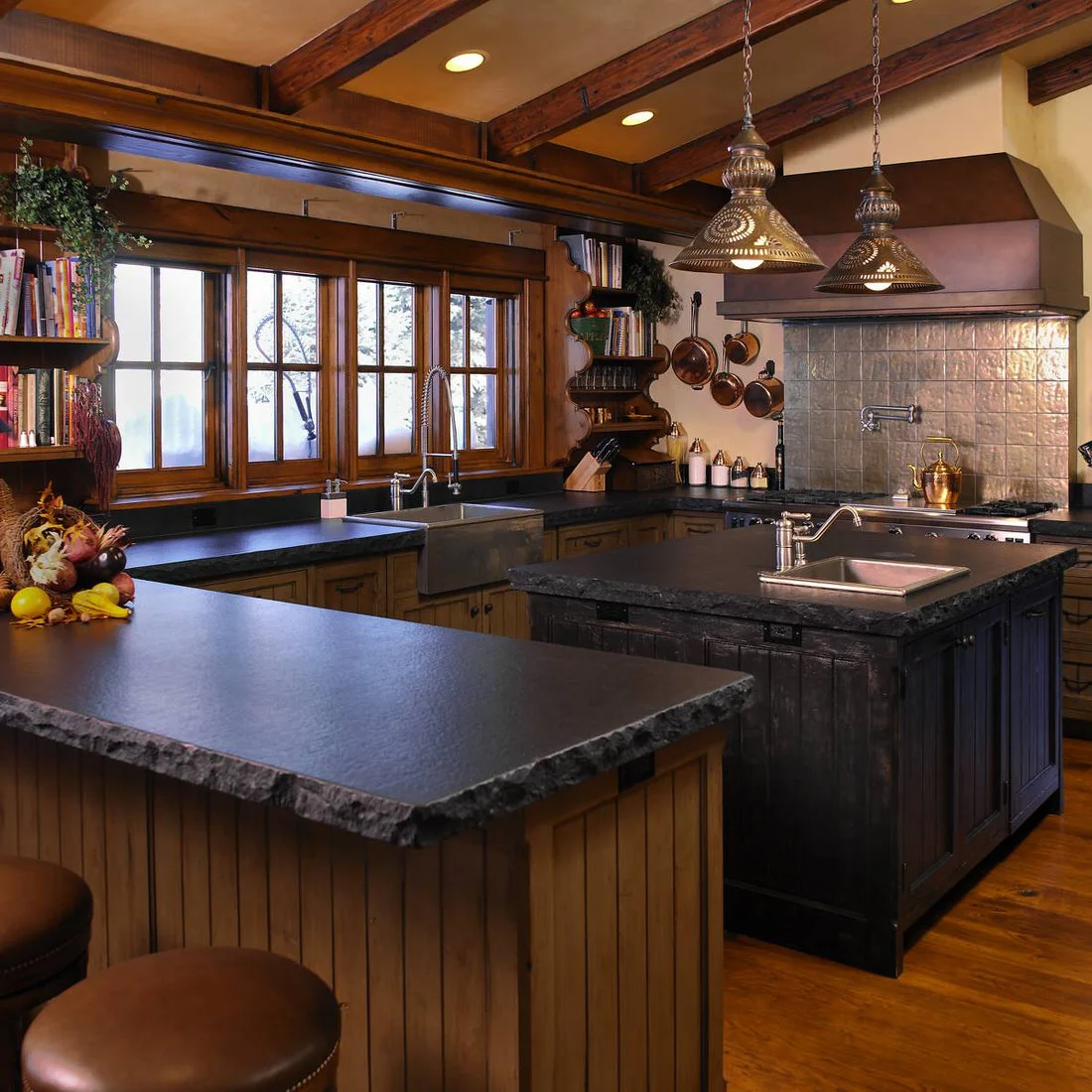A rustic kitchen with timber beams, dark island, hanging pans and pierced pendant shades