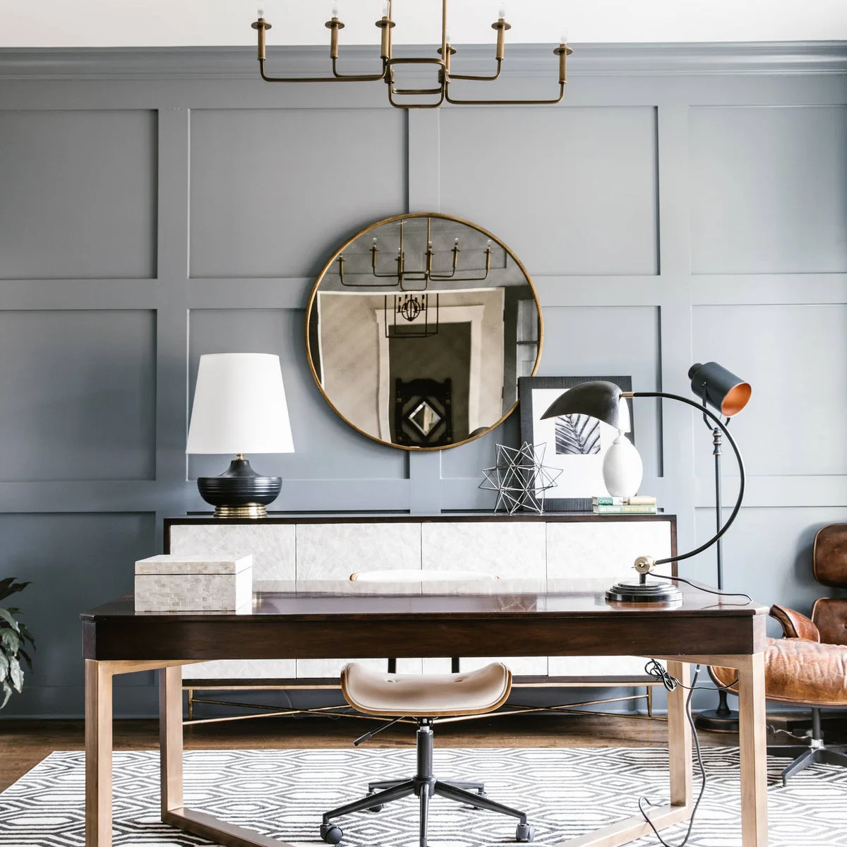 Blue-gray rectangular wall paneling behind a desk, round mirror and sideboard