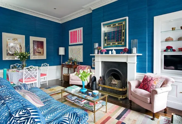 Vivid blue walls frame a pale fireplace beside patterned seating and a pink chair.