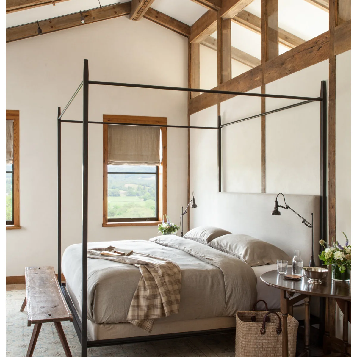 Narrow rustic wooden bench in front of a dark four-poster bed and exposed beams