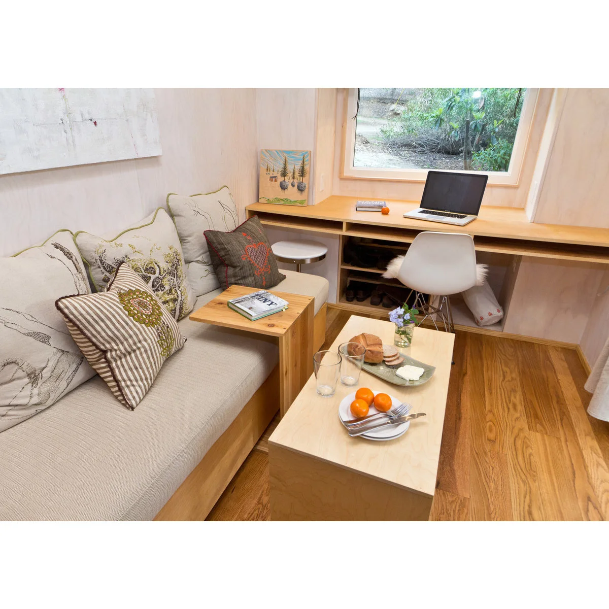 Pale built-in sofa used as a guest bed beside a wood desk and a movable rectangular table