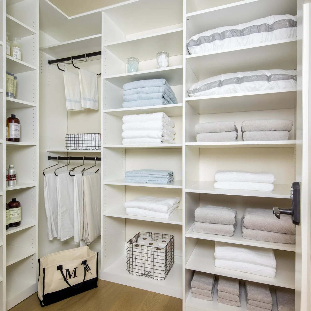 White walk-in linen storage with folded towels, spare pillows and two rods holding pale flat textiles