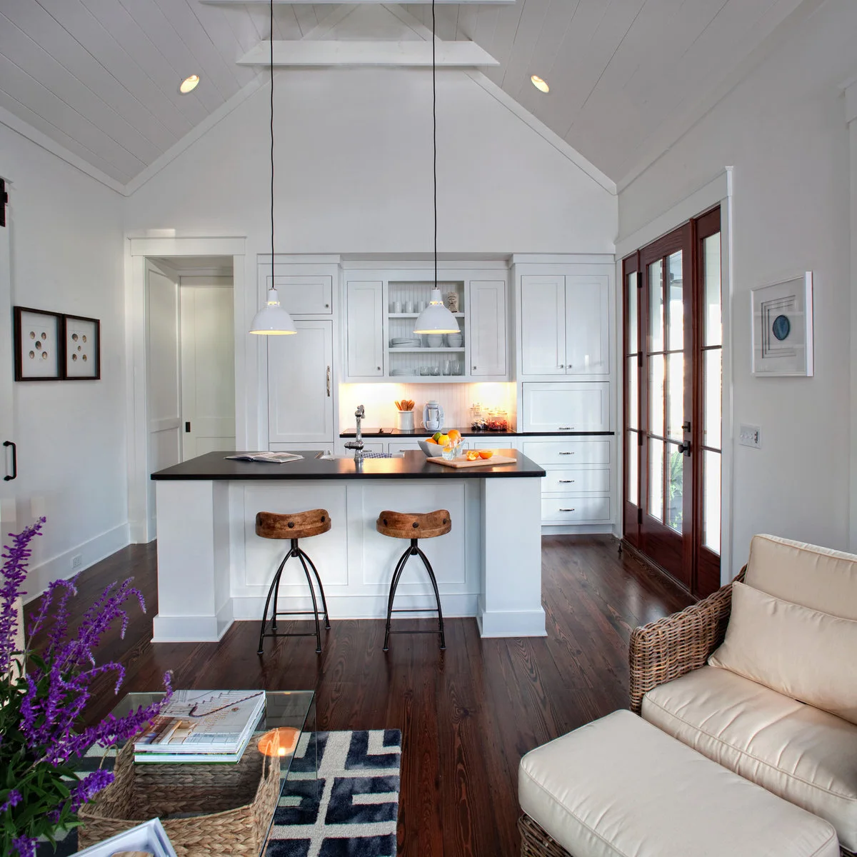 Compact white kitchen with a two-stool island beside glazed doors and a wicker armchair
