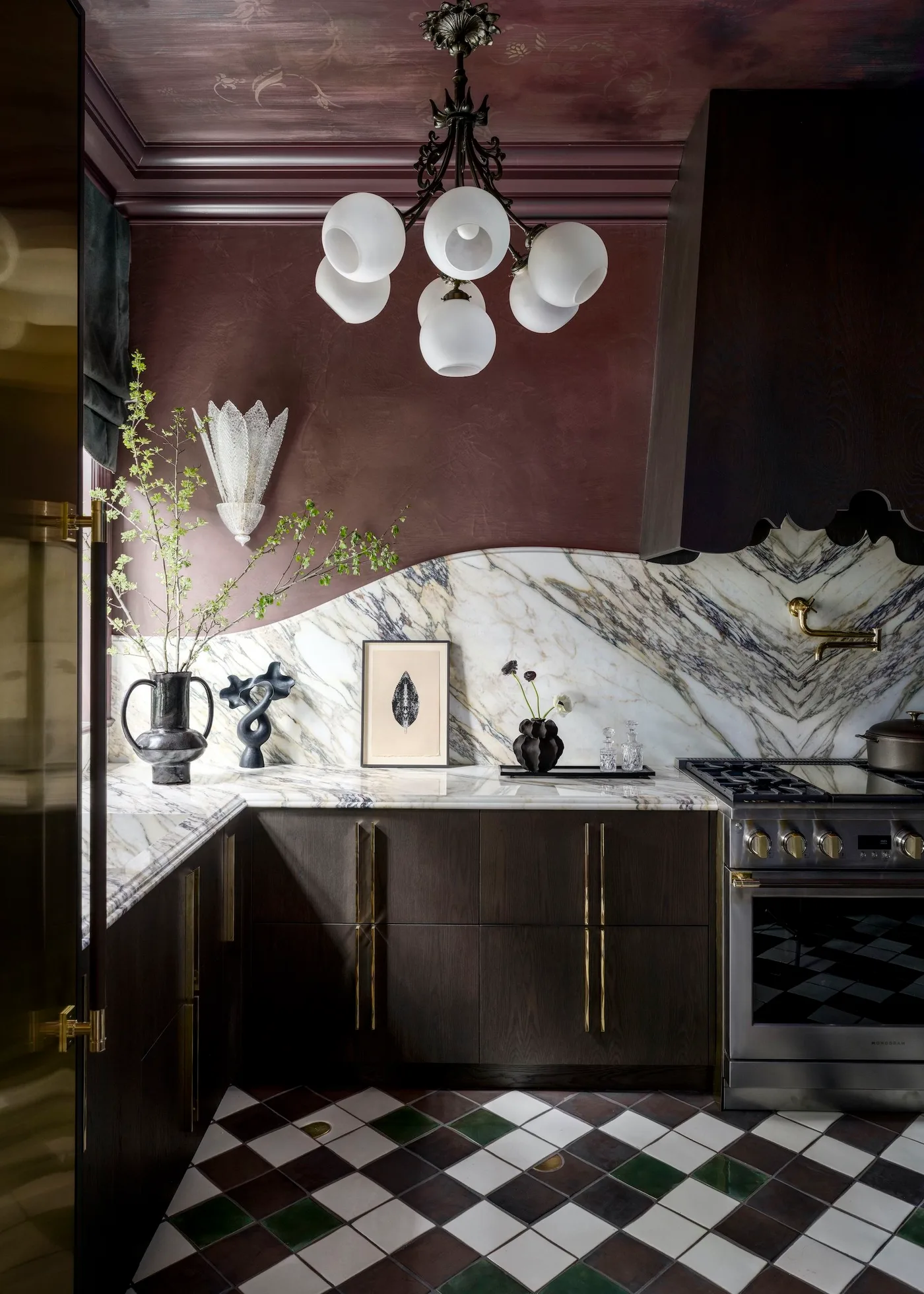 Dark brown lower cabinets with long warm metal handles, pale strongly veined backsplash, plum-colored walls and ceiling, white globe lighting, and checkered floor.