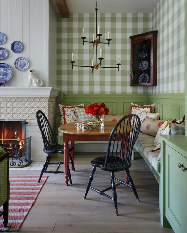 Green lower-wall paneling and corner bench beneath checkered wallpaper beside a small dining table and fireplace