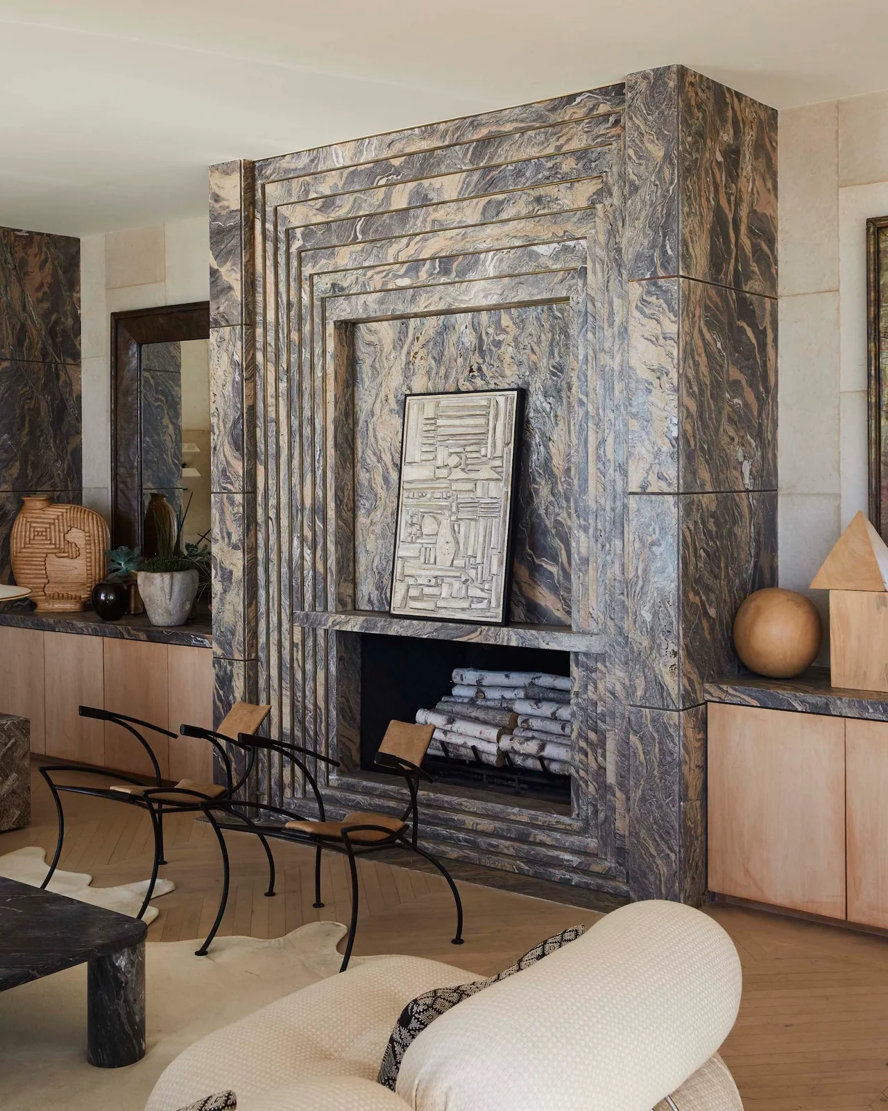 A tall gray-and-white veined fireplace structure has repeated rectangular borders and pale wood storage on both sides