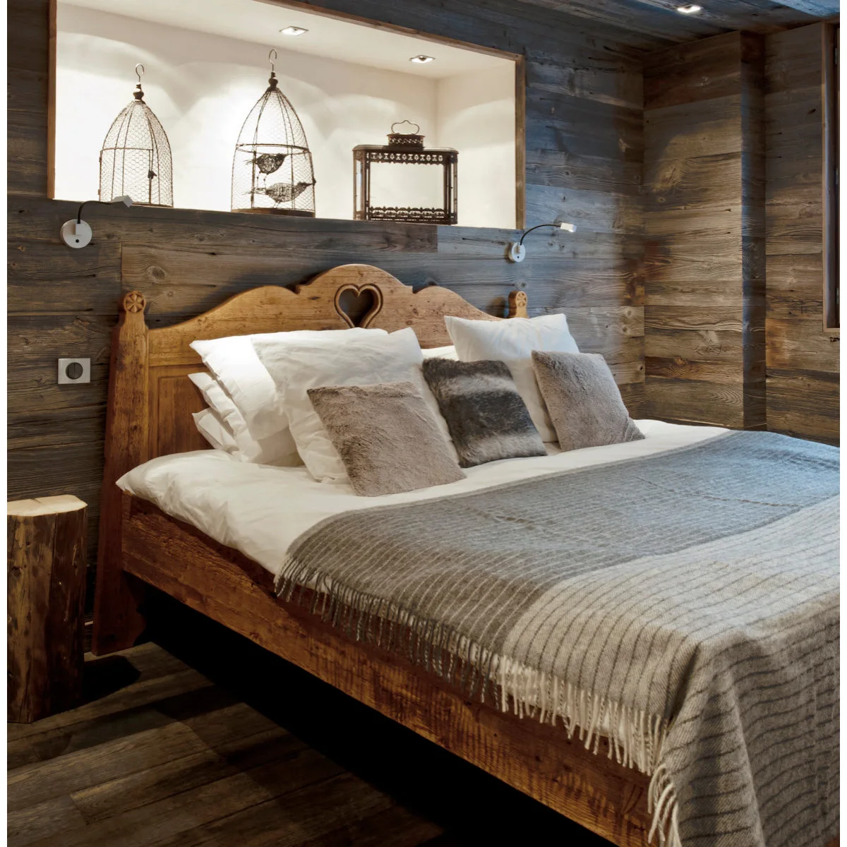 Rustic wood-lined bedroom with heart-cutout headboard, gray throw and two small reading lights