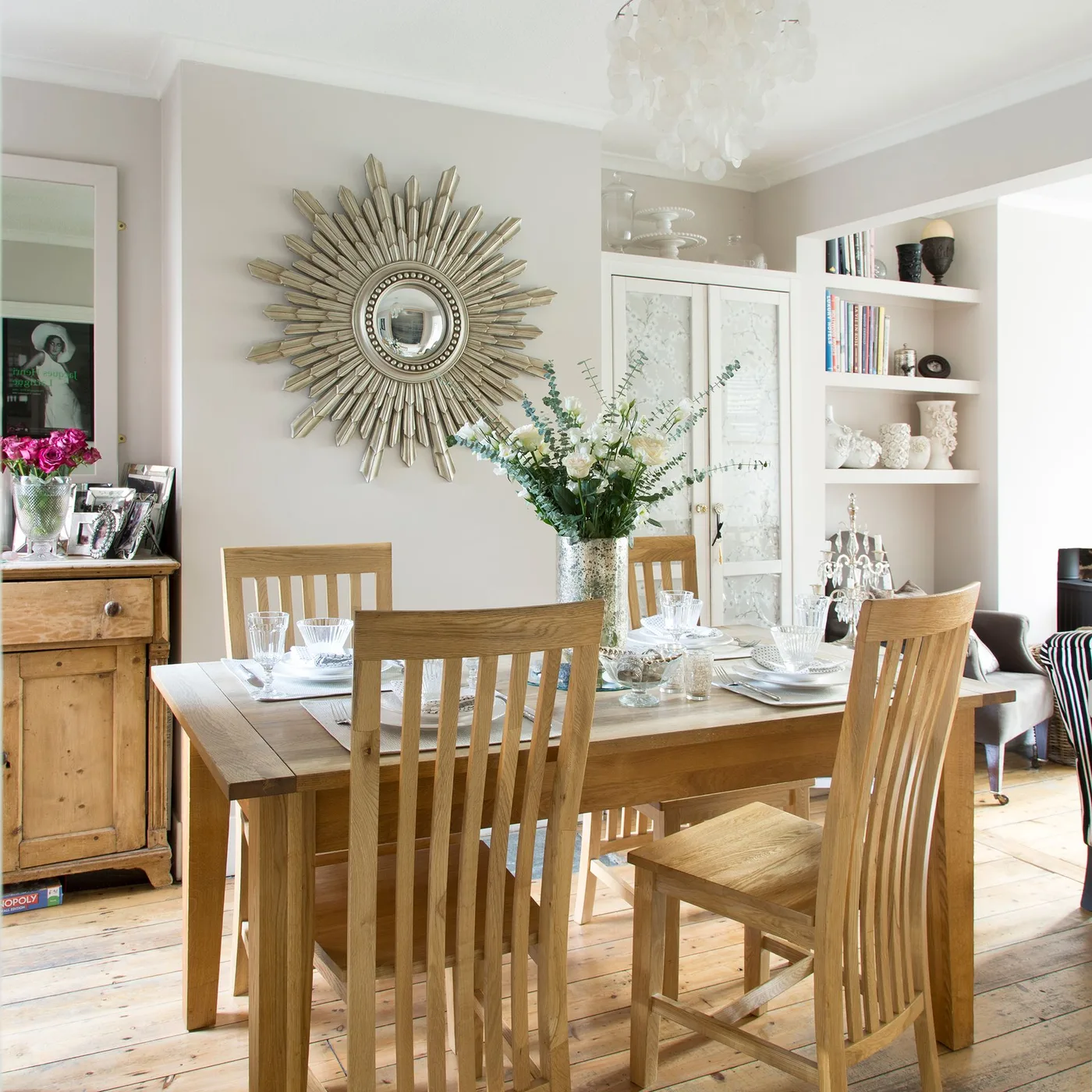 Large metallic sunburst mirror above a wood dining table with tall-back wood chairs and white storage