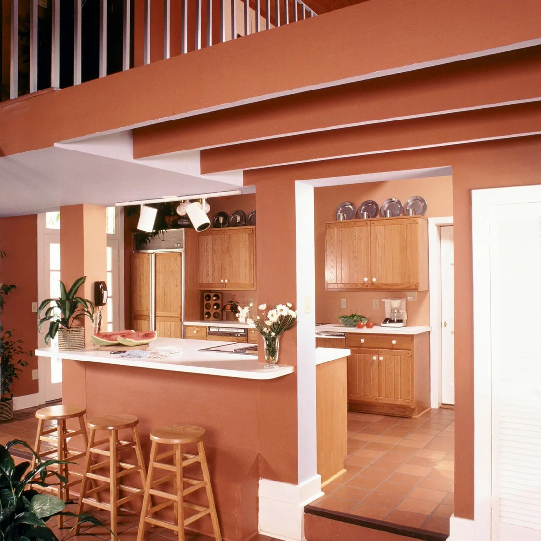 Orange square tiles, peach walls and timber cabinets surround a white-topped breakfast counter.