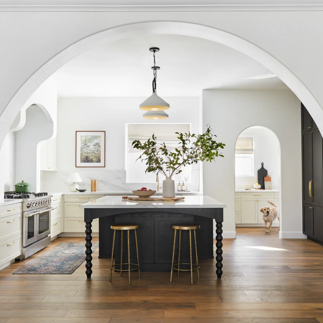 A broad white arch frames a kitchen with pale cabinets, a dark island and a smaller rounded doorway.