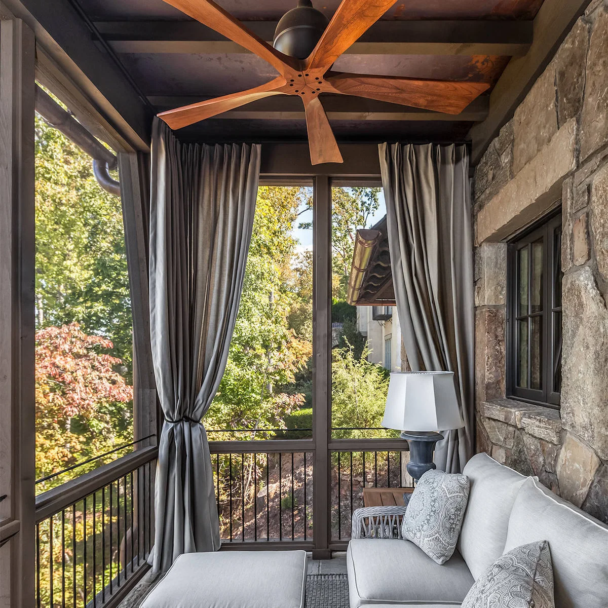 Gray curtains frame a pale sofa on a covered elevated porch with trees outside