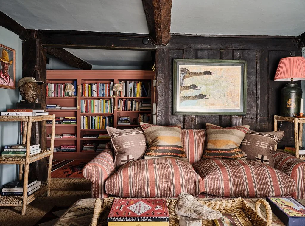 Rust-red striped sofa with patterned cushions, dark timber walls and a bookcase behind