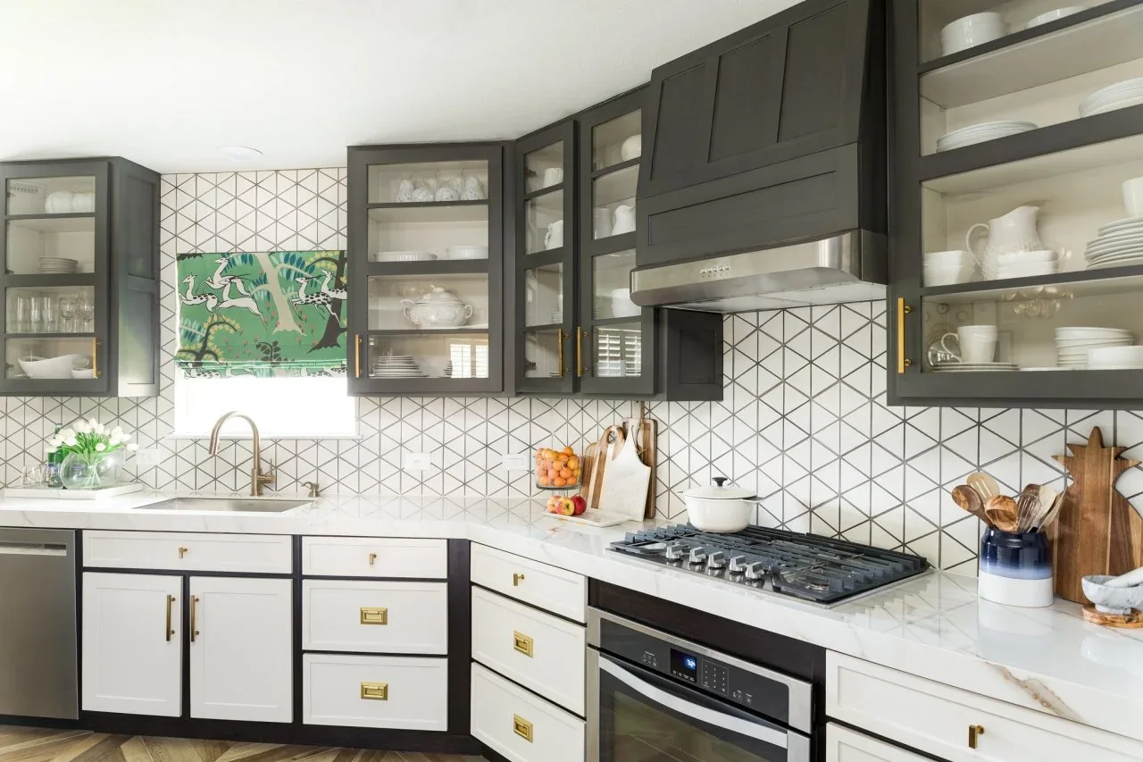 Black upper cupboards and dark lower cabinet frames surround white lower doors, with a geometric pale backsplash and gold-colored hardware.