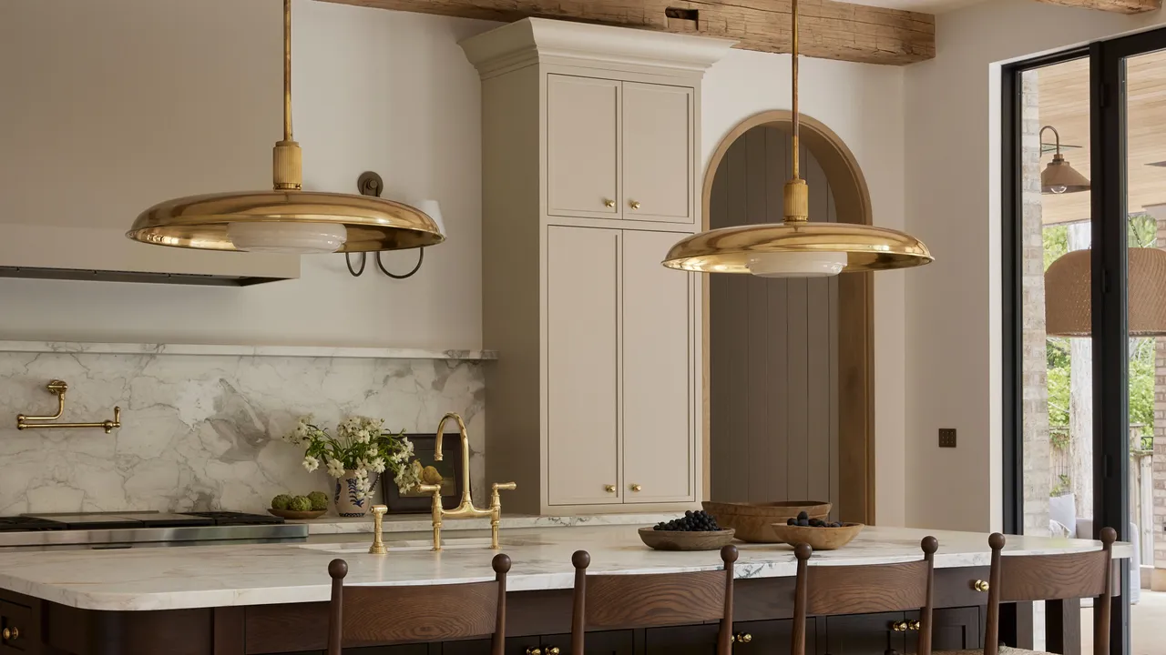 Beige paneled cabinets sit behind a marble-look counter and wide brass pendants