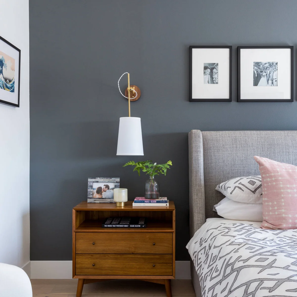Wooden two-drawer nightstand beneath a wall-mounted hanging light on a gray wall