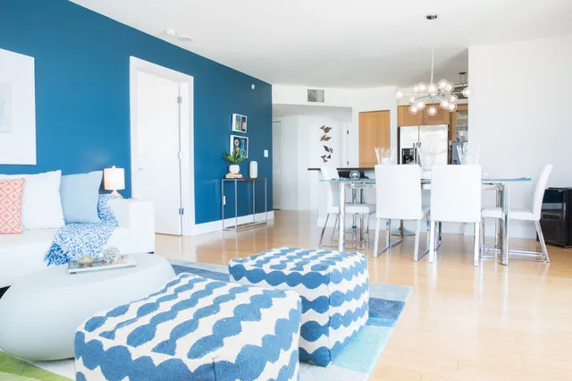 A bright blue wall borders pale furnishings and blue patterned ottomans in an open room.