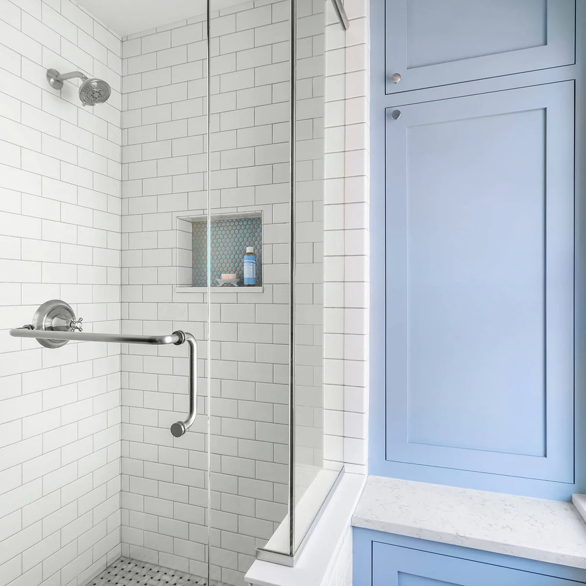 Tall blue cupboard above a counter beside a tiled shower with recessed niche