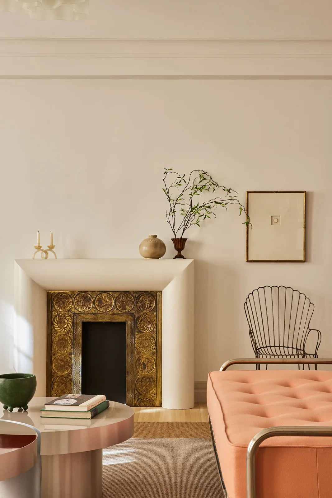 A rounded pale fireplace surround frames a gold-colored patterned inner border beside a peach sofa and open-framed chair