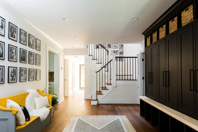 Yellow bench with pale cushions beneath framed photographs opposite dark entryway cupboards
