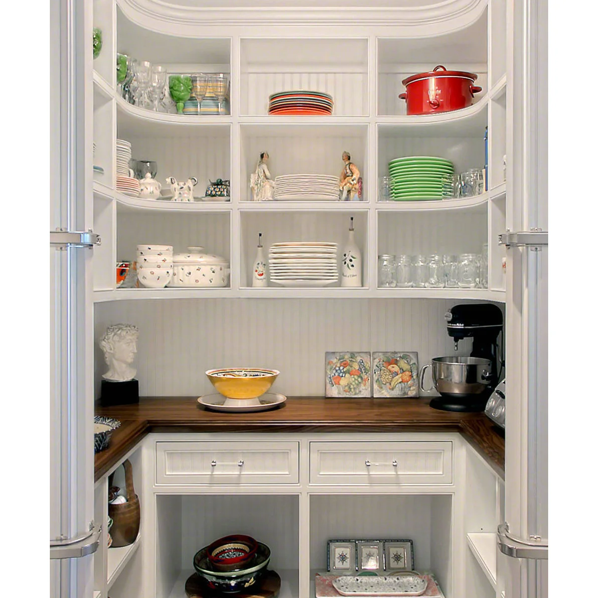 White pantry with curved corner shelves of plates, glasses and serving dishes