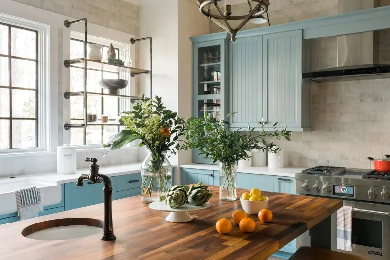 Pale blue cabinets surround a striped timber island top with a small round sink and dark tap.