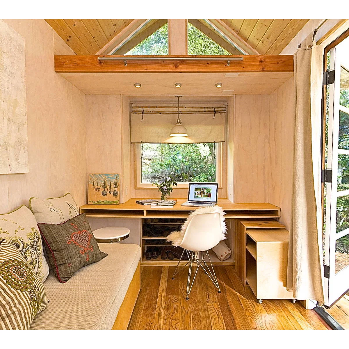Small wood-lined garden office with fitted desk, sofa bench, white chair and mobile storage unit