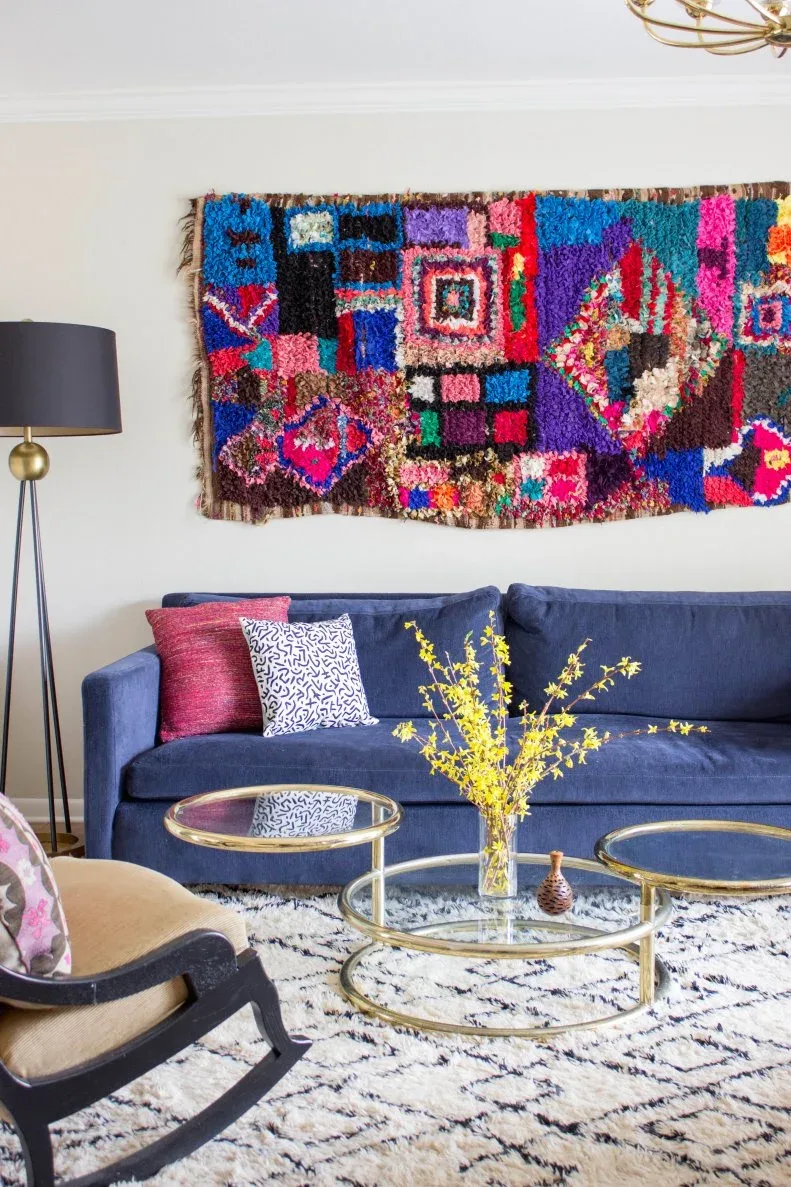 Blue sofa beneath a bright patchwork-style wall textile with two round gold-colored tables.