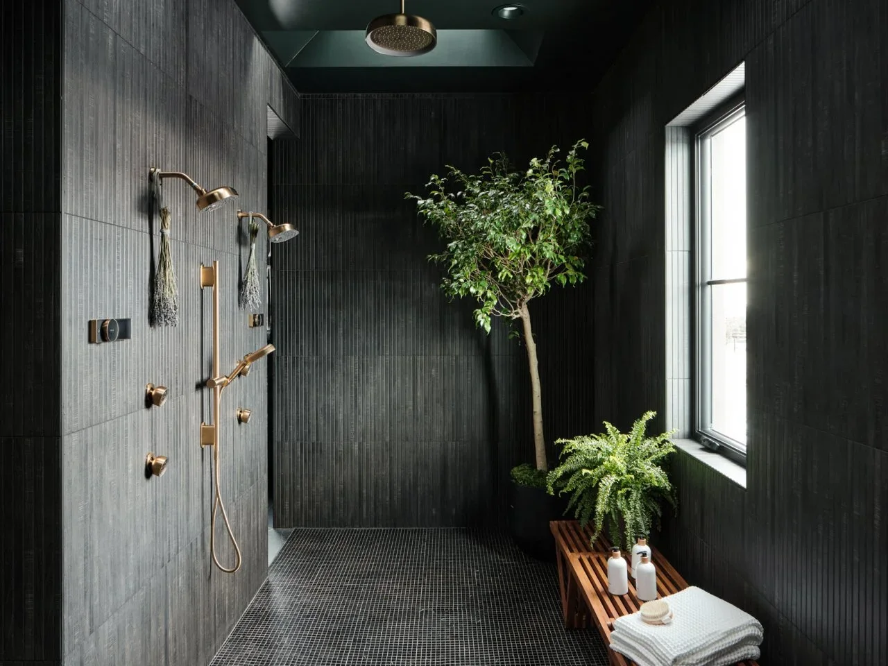 Greenery and a timber bench stand against dark ribbed shower walls beside a tall window.