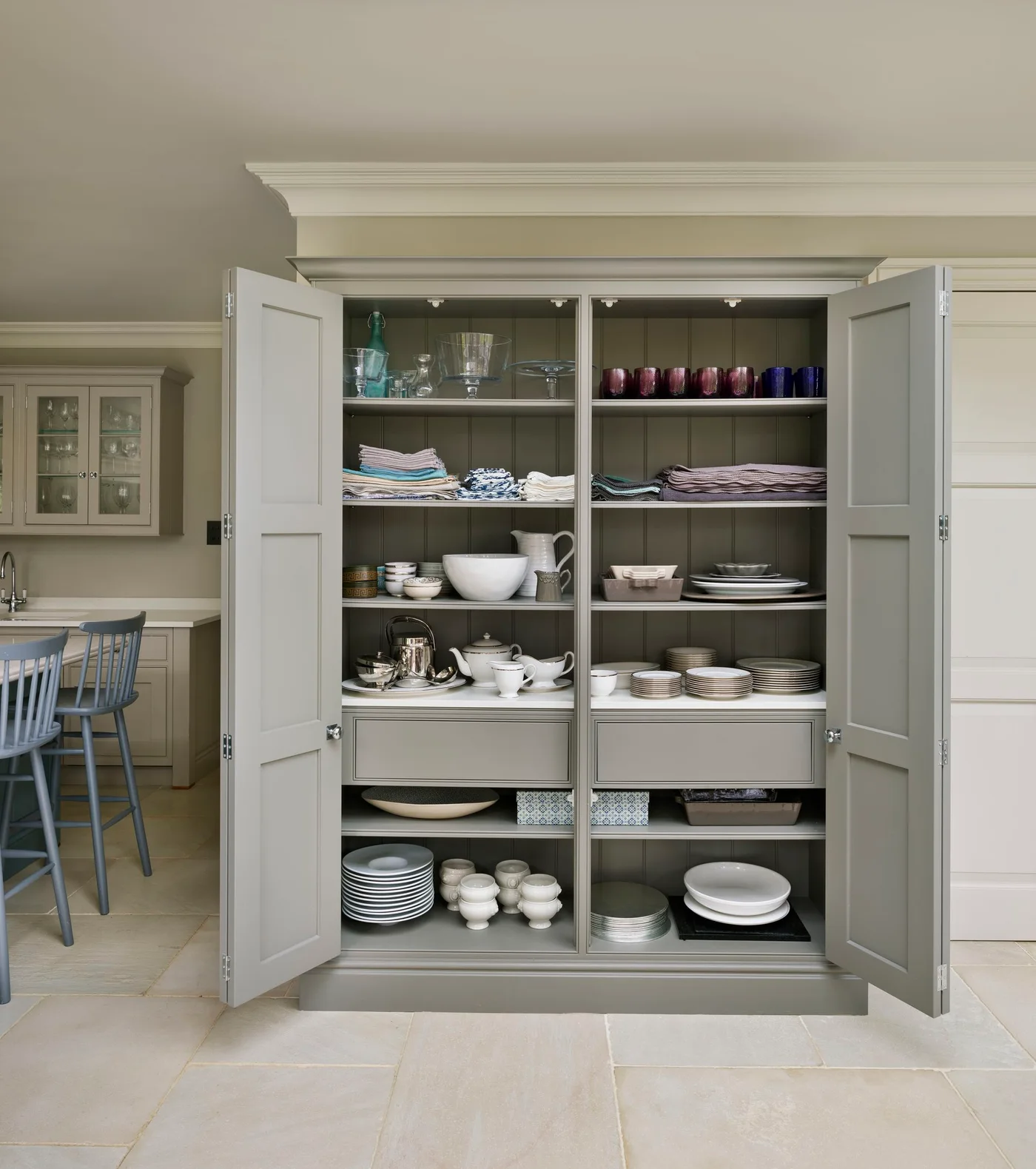 Tall cupboard with folded table linens, glasses, plates and serving pieces