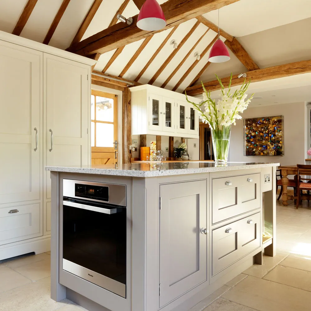 Cream perimeter cabinets and a gray island sit beneath exposed timber roof beams