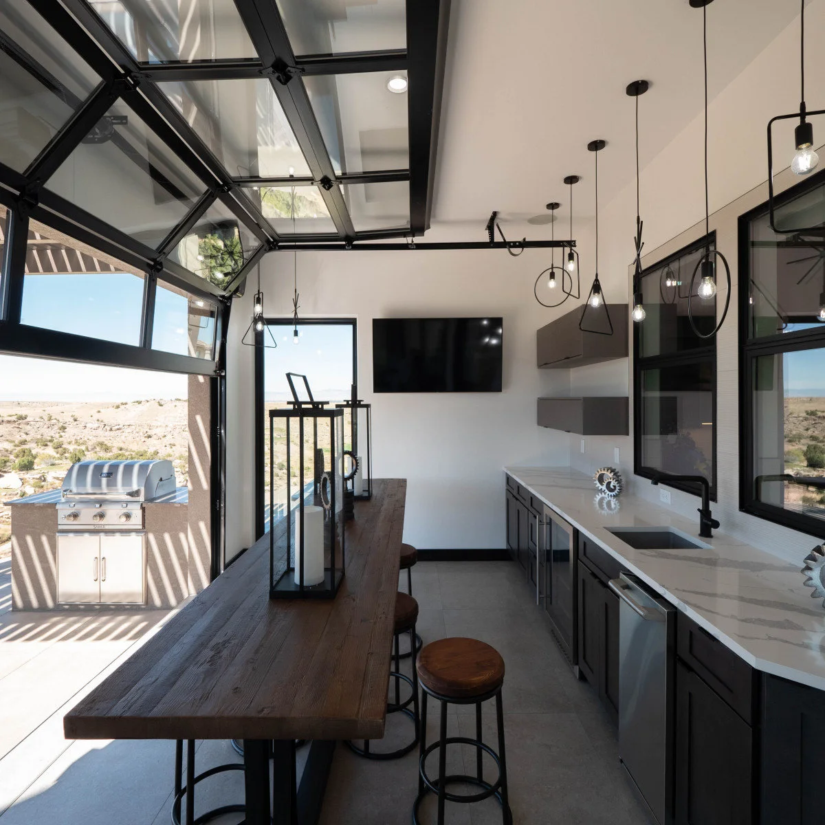 Serving room with sink, dark cabinets and wood counter beside a wide opening toward an outdoor grill