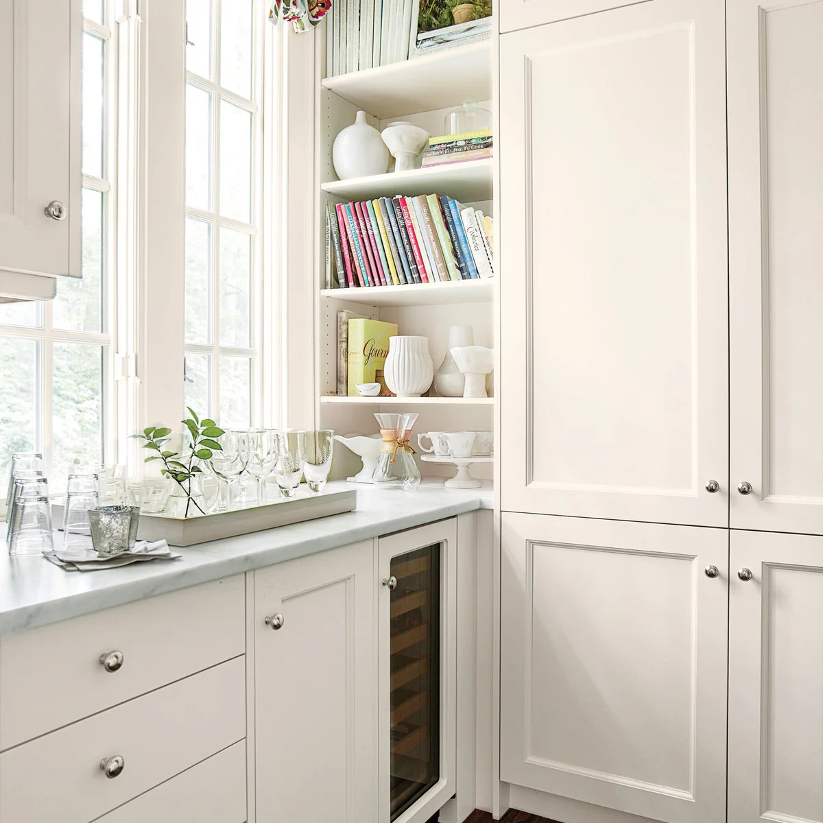 White kitchen with a slim open book shelf between a window counter and tall cupboards