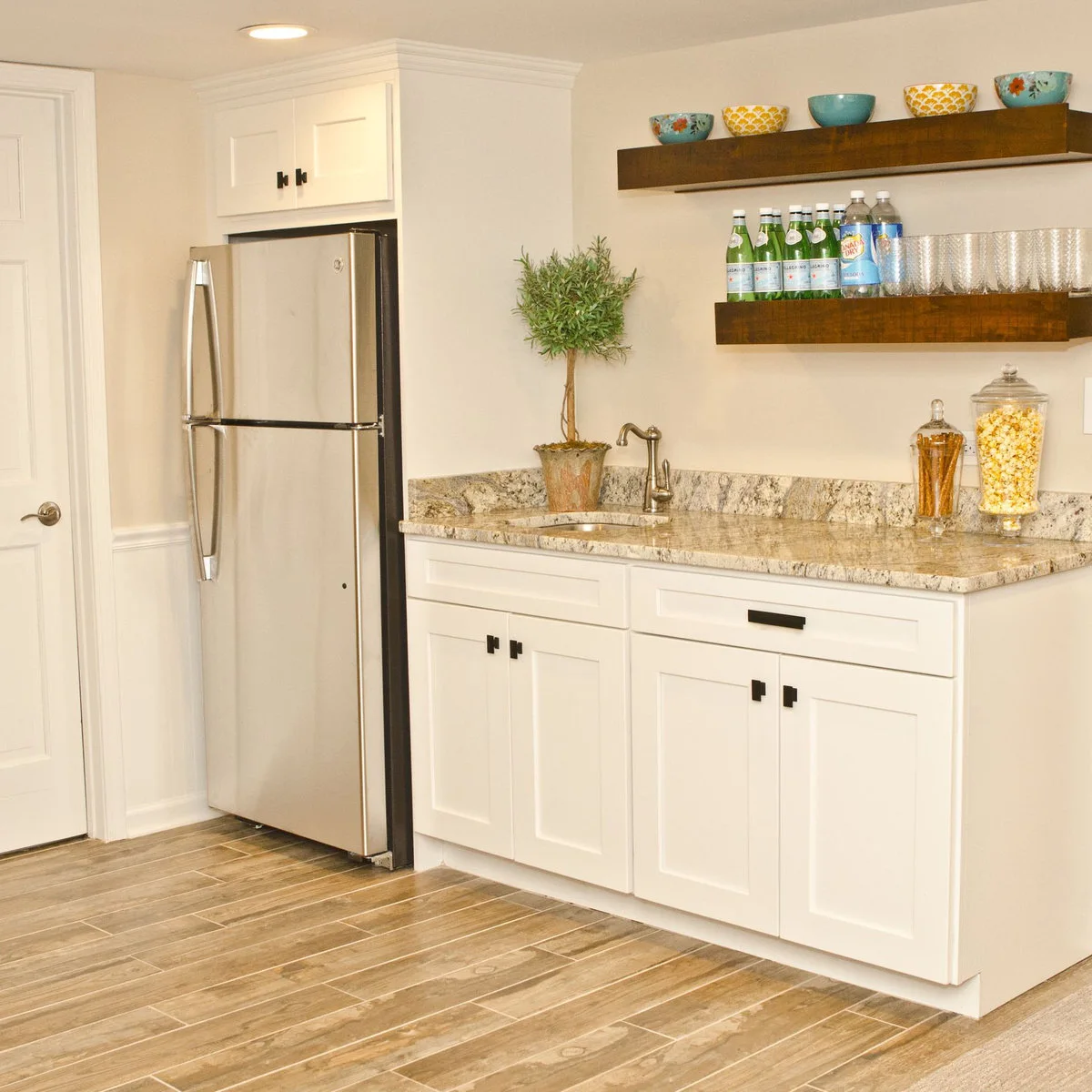 Short white kitchenette with a refrigerator, sink and open wood shelves