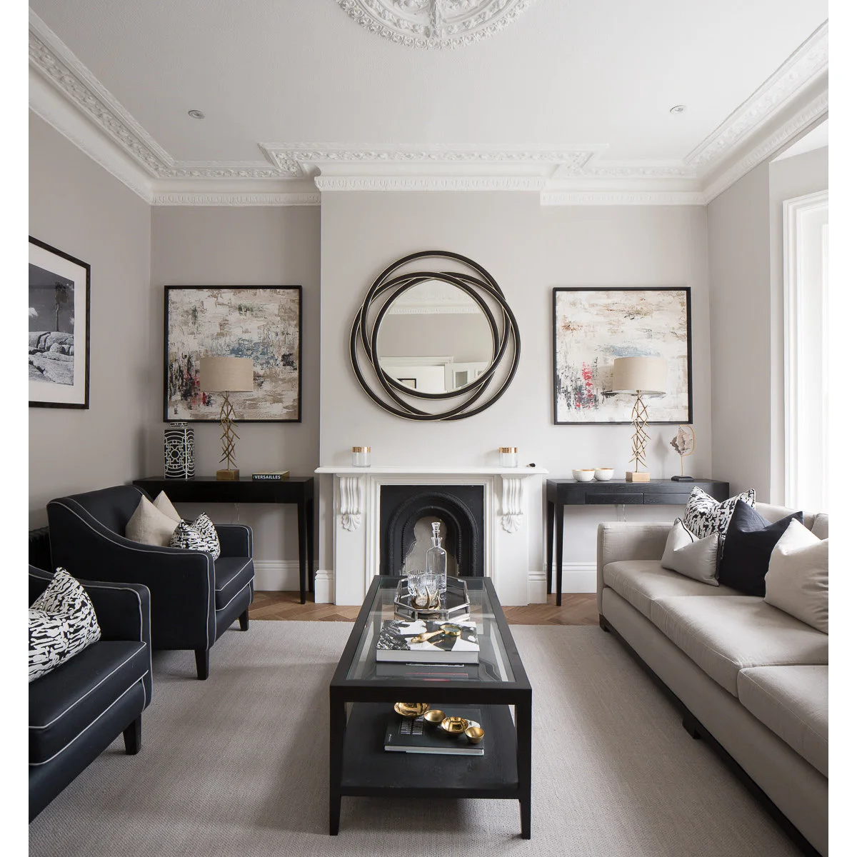 Pale front room with two dark chairs, narrow black consoles and glass-topped coffee table