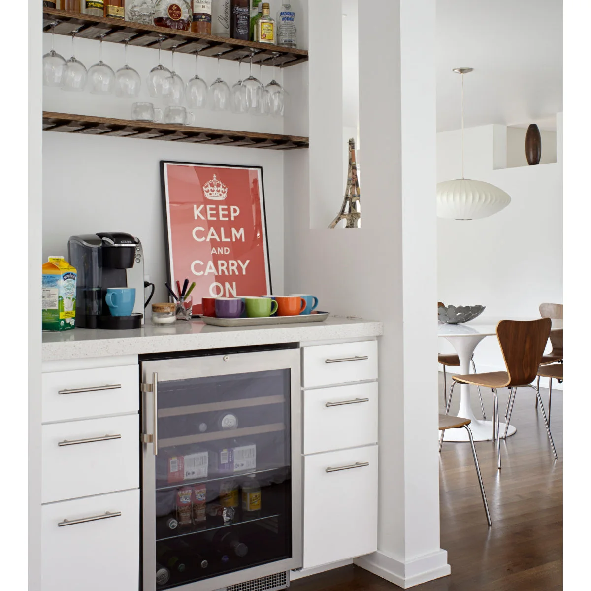 Compact white beverage counter with coffee maker, colorful cups on a tray and a small fridge below