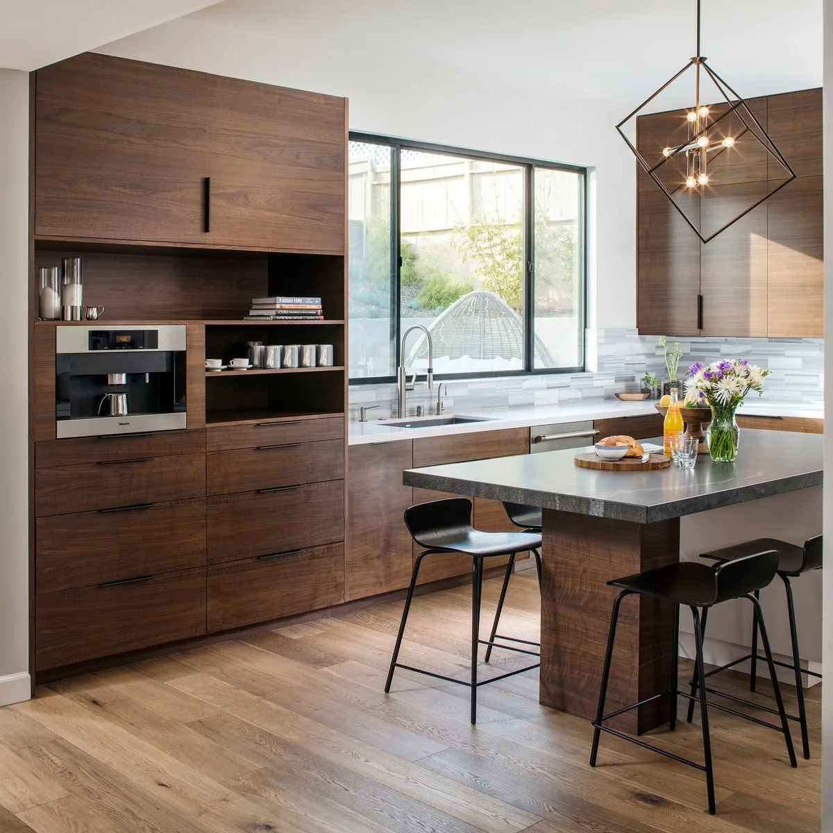 A tall wood cabinet with an integrated coffee appliance and open cup shelves beside a window sink and small island.