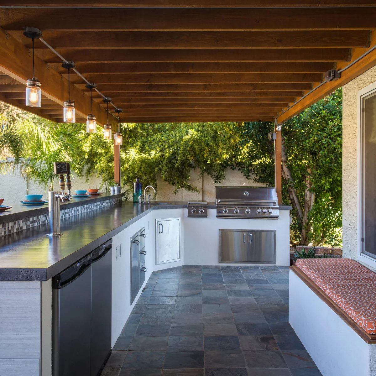 Outdoor bar with a raised ledge, beer tap, small sink, lower cabinets and refrigerator beneath timber rafters